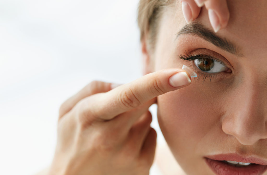 Young woman puts contact lens in her eyes.