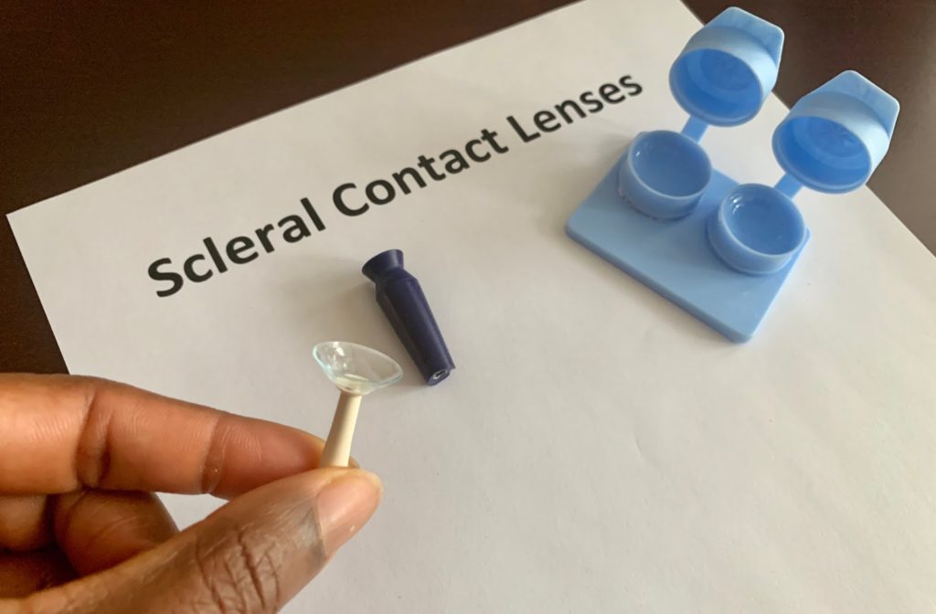 Hand holding scleral contact lens above a sheet of paper marked "scleral contact lenses"