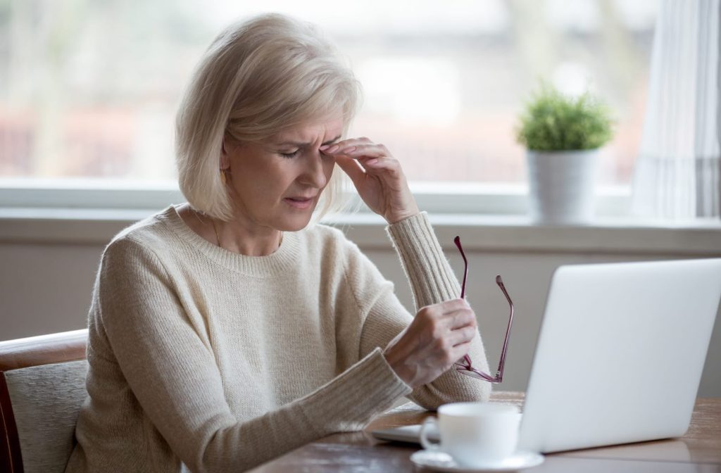An older woman sits at a computer rubbing her eyes due to severe dry eye symptoms