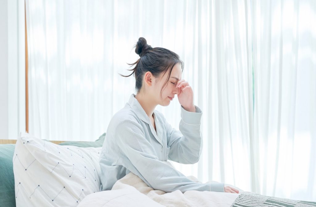 Young woman laying in bed touching her eyes due to dry eyes.