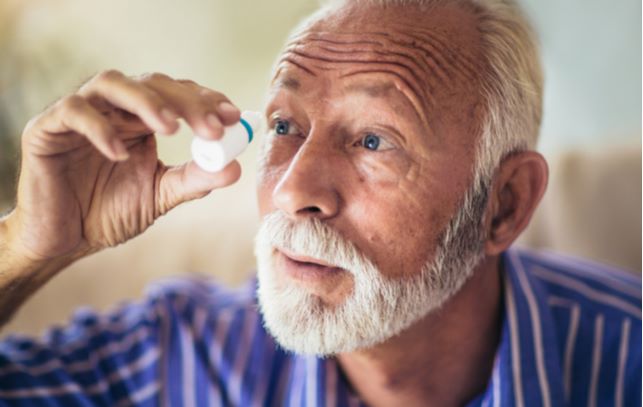 Elder man putting in eye drops caused due to dry eyes from winter months