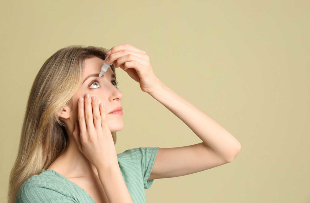 A young woman's holding an eye drops near her right eye.