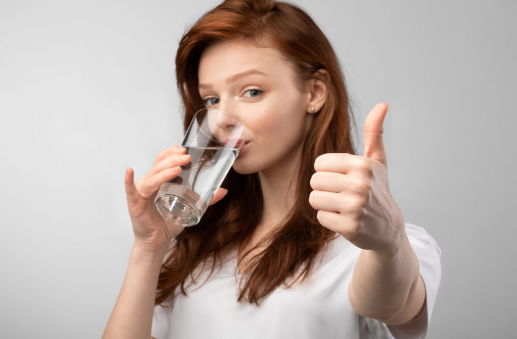 A young girl drinking a glass of water does thumbs up.