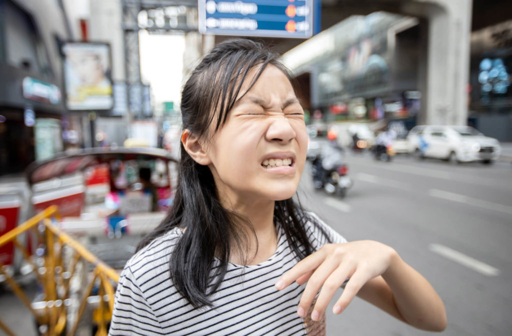 A young girl walking on the streets is suffering from eye irritation due to dust and car smoke.