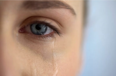Close of a water eye, with a tear running down the person's check.