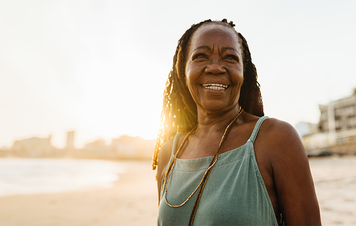 Woman smiling as she stands on beach, with a sun setting in the background.